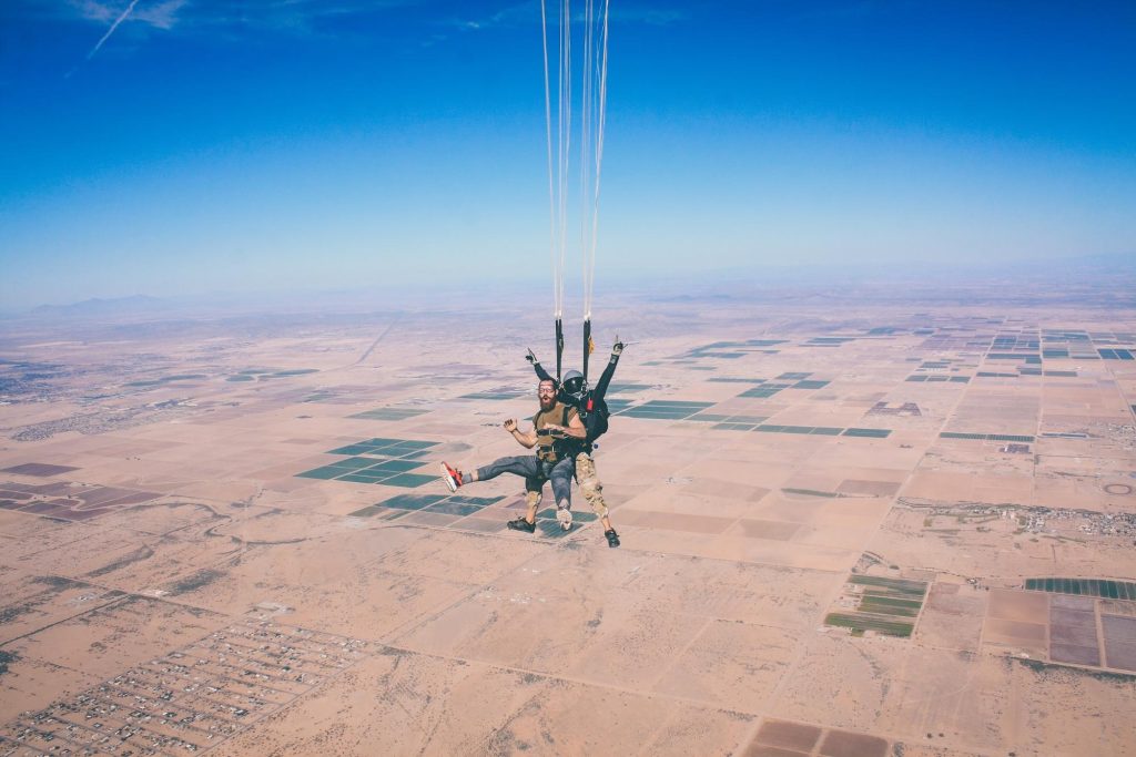 photo of two skydivers connected to each other as they parachute downward